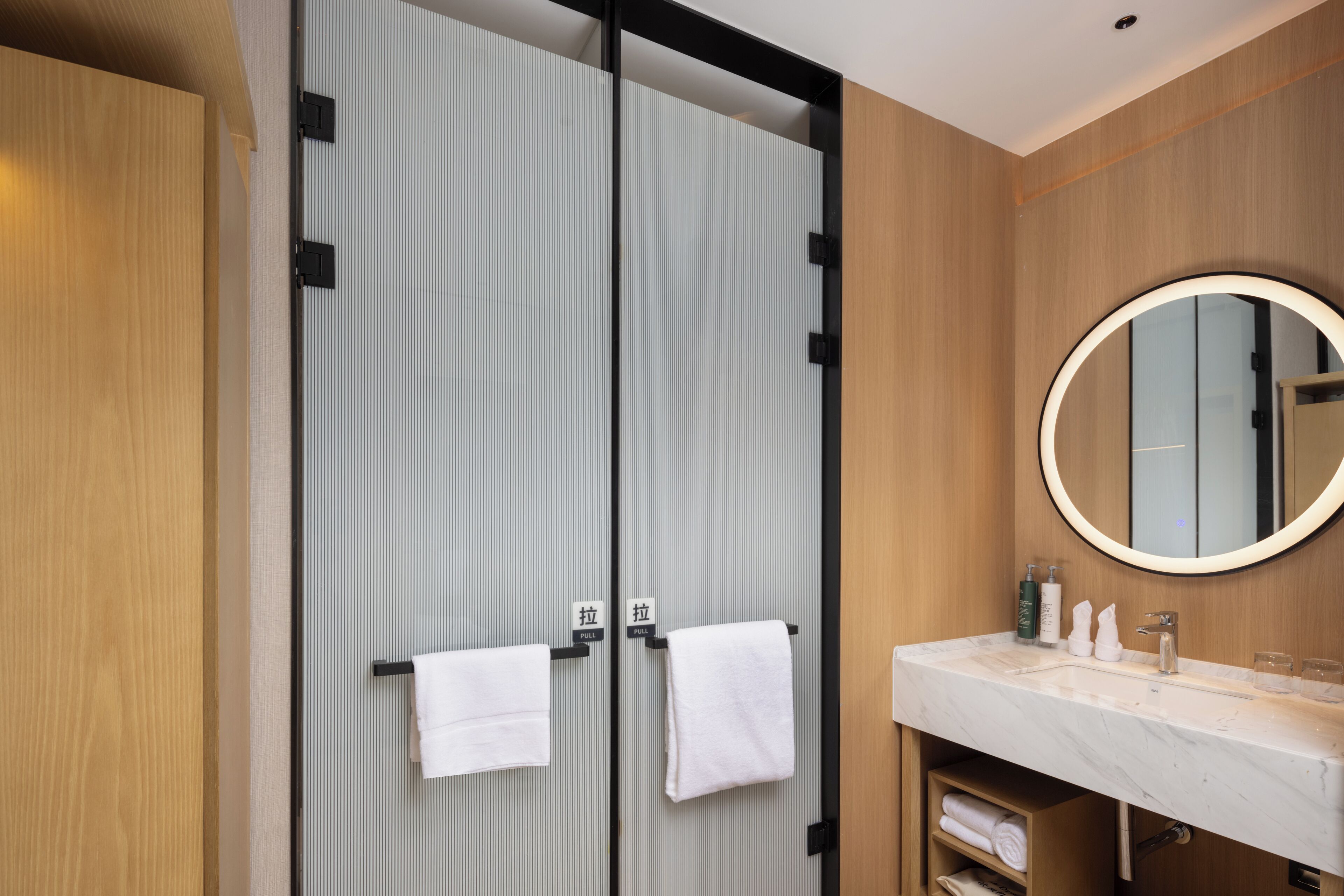 A modern bathroom with a large mirror, two towel hooks, a sink, and a wooden vanity.