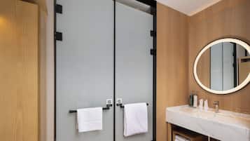 A modern bathroom with a large mirror, two towel hooks, a sink, and a wooden vanity.