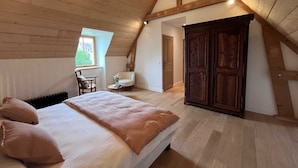 A bedroom with a wooden ceiling, a bed with pillows, a chair, a small table with a vase, and a wardrobe.