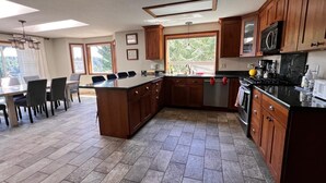 A spacious kitchen with wooden cabinets, a central island, and a dining area with chairs. - Waterfront charming 3-bedroom house with hot tub, sauna and bikes, sleeps 6 (Shelton)
