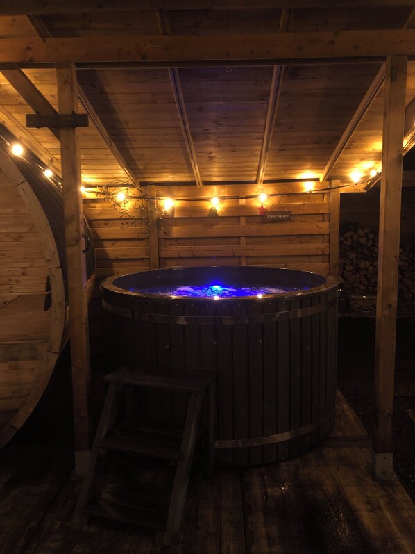 A wooden cabin with a hot tub under a sloped roof, surrounded by wooden walls and a wooden deck.