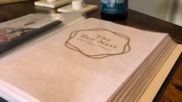 A table with a placemat labeled "The Zen Nest Wellness Chalet," a bottle of Miel Perle, two glasses, and two lit candles.