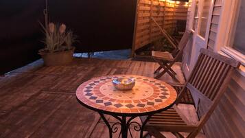 Een houten terras met een mozaiektafel en stoelen, een potplant en lichtjes.