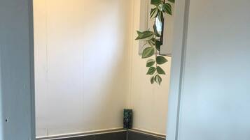 Une petite salle de bain étroite, avec des toilettes, des murs recouverts de carreaux sombres et une seule plante verte accrochée au mur.
