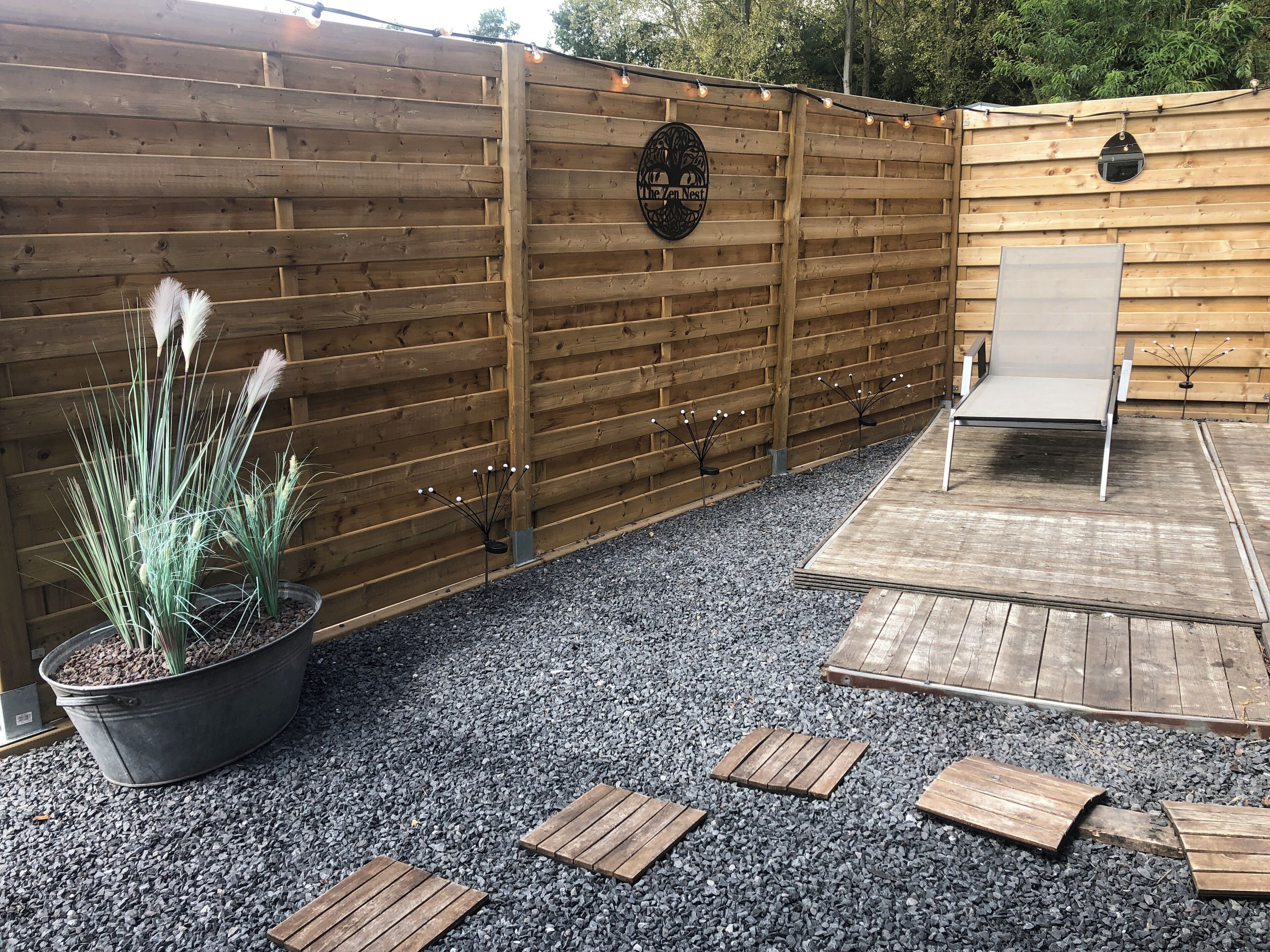 A wooden fence with a sign, a potted plant, and a wooden deck with a chair.