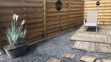 A wooden fence with a sign, a potted plant, and a wooden deck with a chair.