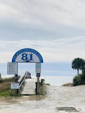 Entrada a la playa con un letrero que dice "BAY COUNTY PUBLIC BEACH ACCESS" y un aviso sobre las corrientes marinas.