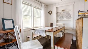 A dining area with a wooden table and chairs, a white wall with shelves holding plates and a lantern, and a window with blinds. - Modern Family Home in Laguna Beach! 4-block Walk to Beach + Pet Friendly! (Panama City Beach)