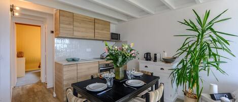 Una cocina moderna con armarios de madera, una mesa de comedor preparada para cuatro personas y una planta verde grande.