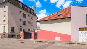 A street view with a building featuring a red roof and a beige facade.