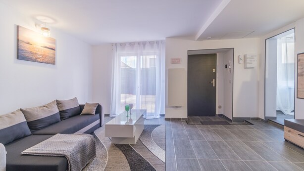 A modern living room with a sofa, a coffee table, and a view of the outside through sheer curtains.