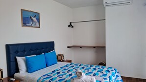 Un dormitorio con cama, una lámpara colgante, aire acondicionado instalado en la pared y un cuadro con una ballena.
