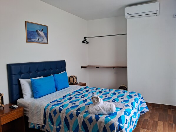 Une chambre à coucher comprenant un lit, une lampe suspendue, un climatiseur fixé au mur et un tableau représentant une baleine.