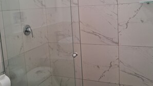 Un box de ducha con paredes de cristal, un cabezal de ducha manual y un grifo empotrado.