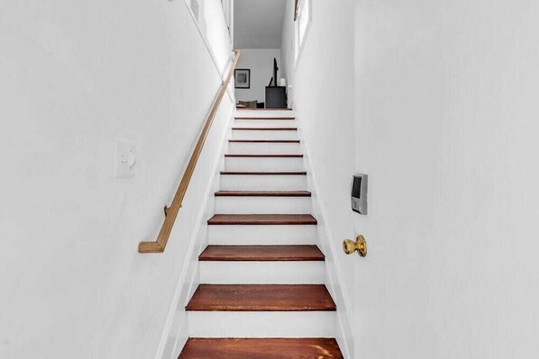 Una escalera de madera con barandilla de latón que conduce a un rellano con un objeto negro y un marco de fotos.