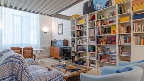Una sala de estar con un sofá, una mesa de centro, una estantería y un televisor.