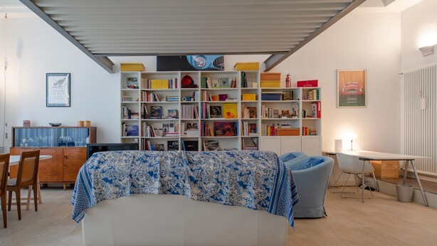 Una sala moderna con un sofá, una estantería, un comedor y una pequeña mesa.