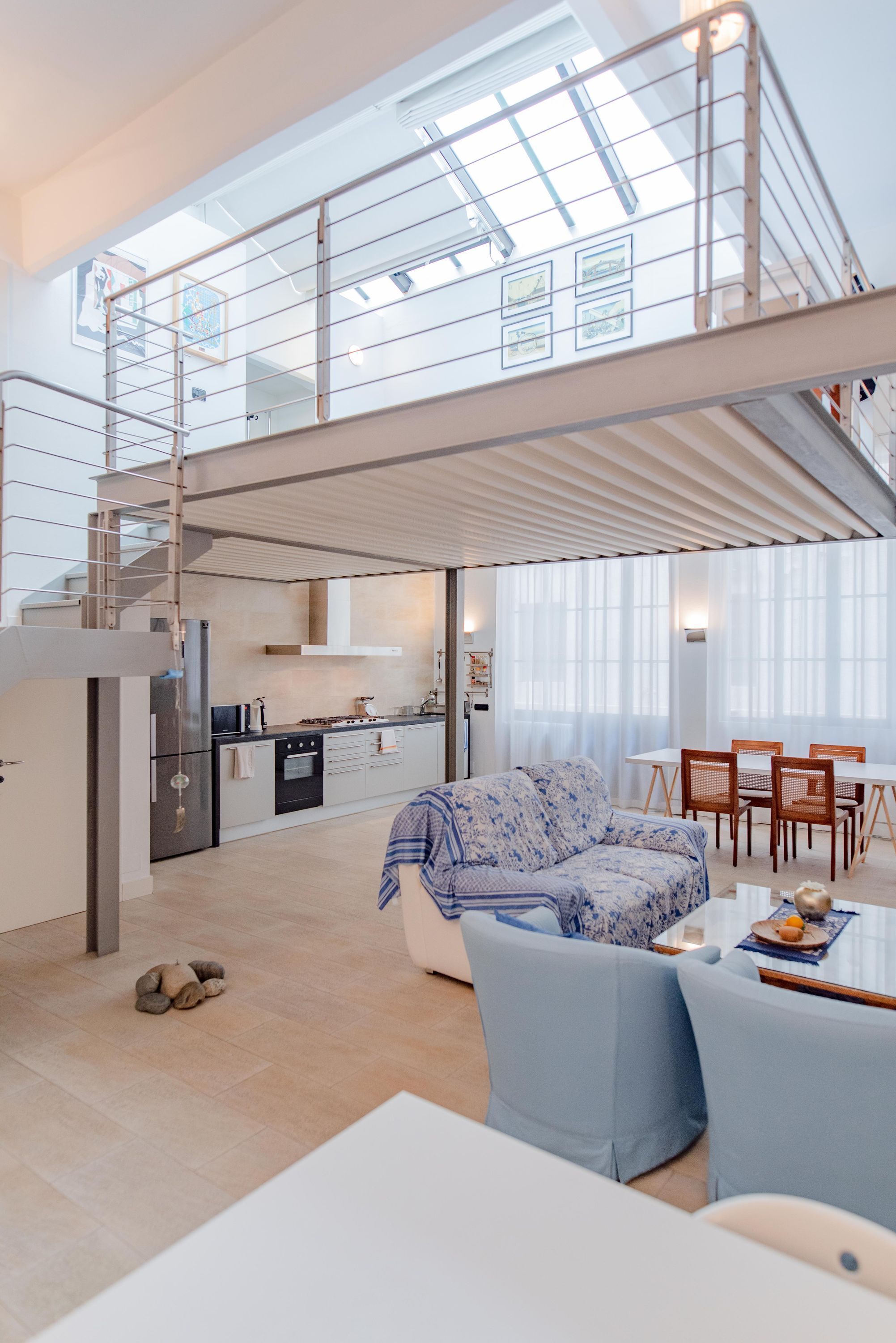 A spacious living area with a high ceiling, a mezzanine level, and a kitchen area.
