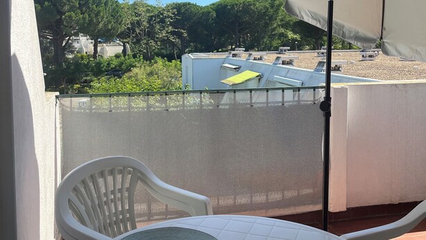 Un balcon avec une table blanche et deux chaises, un parasol et une vue sur un paysage verdoyant.