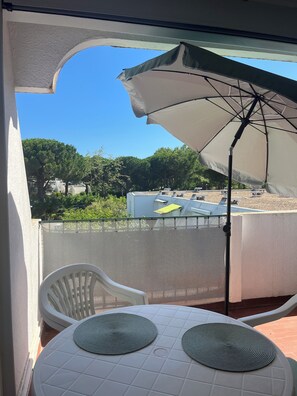 A balcony with a white table and two chairs, an umbrella, and a view of a green landscape.