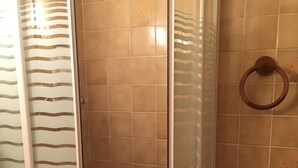 Un espace douche doté d’une porte en verre, de murs carrelés, d’un lavabo blanc et d’une petite étagère avec un panier.