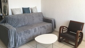Un salon avec un canapé gris, une chaise en bois et une petite table blanche.
