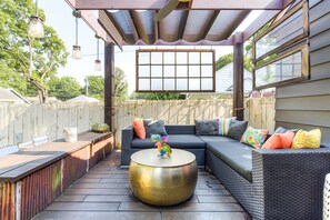Eine Terrasse im Freien mit Korbmöbeln, einem runden Tisch und einer Pergola darüber.