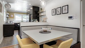 Moderni keittiö, jossa on kiinteä keittiösaareke, ruokailutila pöydän ja tuolien kera sekä seinällä oleva kello.