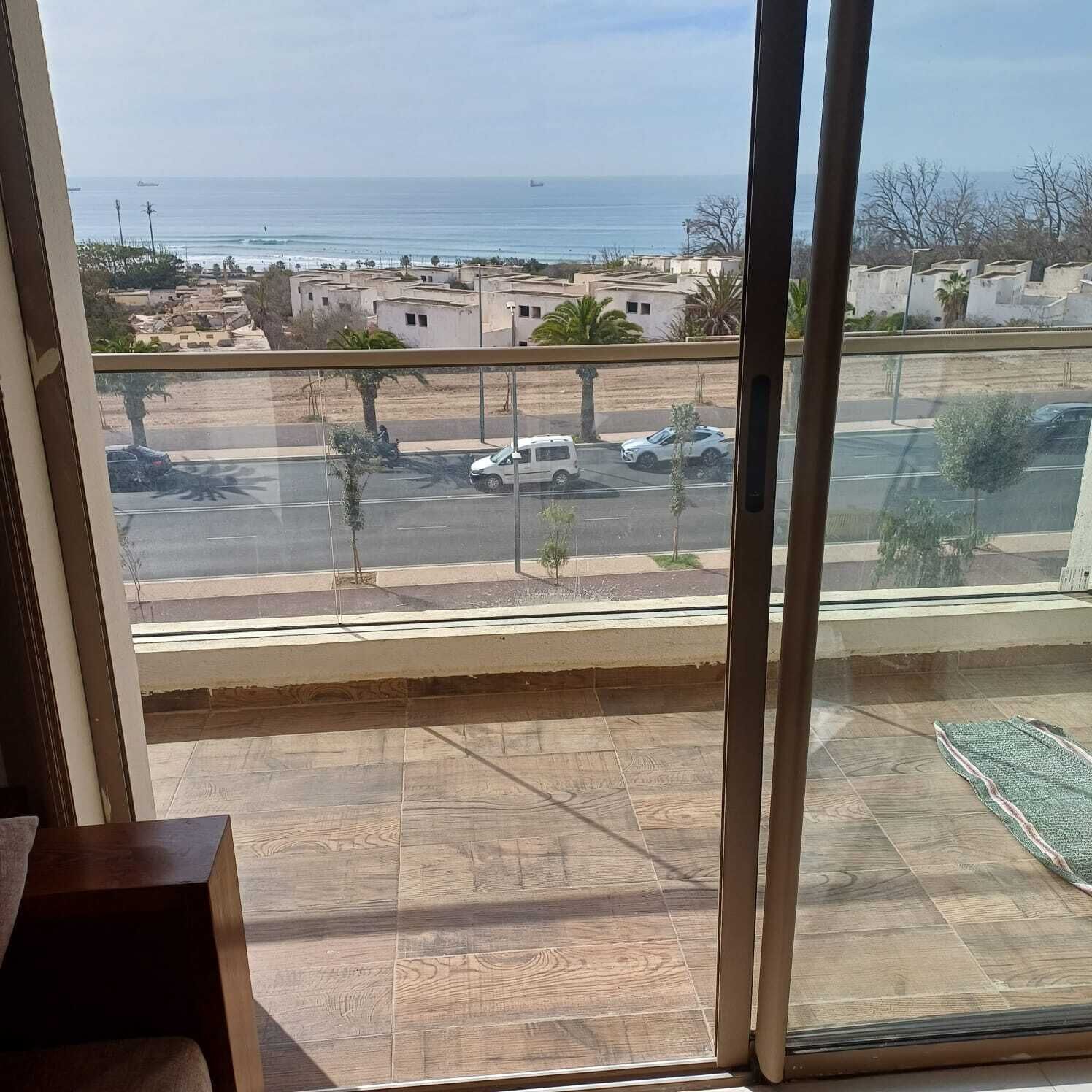 A view from a balcony with a clear view of the sea and a parking area with several cars.