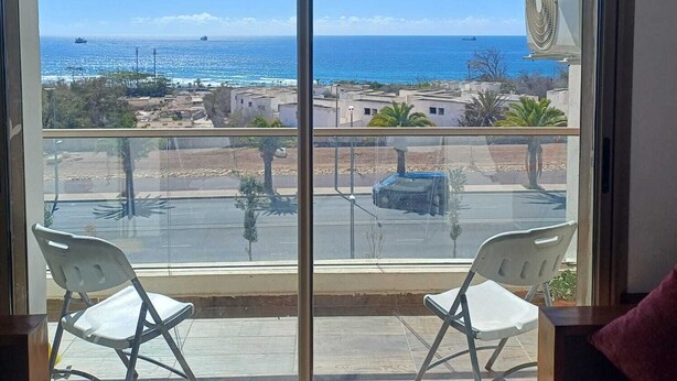 A balcony with two white chairs, a view of the sea, and a large air conditioning unit. - Sea House Agadir (Agadir)