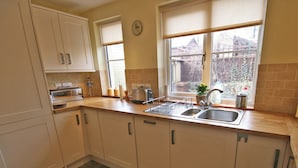 A kitchen with white cabinets, a double sink, a window with a view of the outside, and a clock on the wall. - 2 bedroom accommodation in Warkworth (Warkworth)
