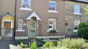 A two-story house with a brick exterior, a green door, and a small garden with various plants. - 2 bedroom accommodation in Warkworth (Warkworth)