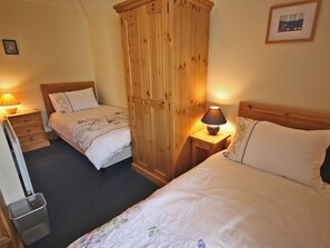 Une chambre avec deux lits, une armoire en bois, des tables de chevet avec des lampes et un tableau encadré au mur.
