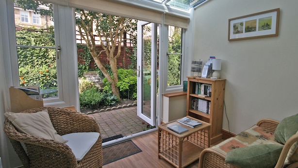 A sunlit room with a glass door leading to a garden, wicker furniture, and a bookshelf. - 2 bedroom accommodation in Warkworth (Warkworth)