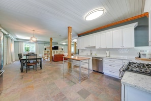 A spacious kitchen with white cabinets, a central island, and a dining area with a table and chairs. - Peaceful Warrenville Home: 1 Mi to Herrick Lake! (Warrenville)