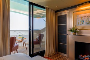 Une chambre d’hôtel moderne dotée d’une porte-fenêtre coulissante donnant sur un balcon, d’un petit coin repas, d’une cheminée et d’une vue sur la mer.