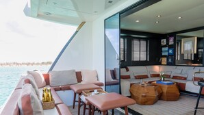 A modern yacht interior with a seating area, wooden coffee table, and a view of the sea. - House of Hütter - Floating Home Goldfinger (Formentera)