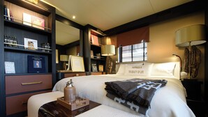 A hotel room with a bed, bedside tables, a desk, a bookshelf, and a large window with blinds. - House of Hütter - Floating Home Goldfinger (Formentera)