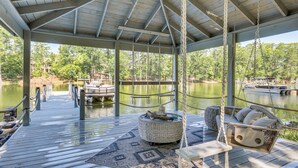 Eine überdachte Holzterrasse mit Schaukelstuhl und gepolstertem Sitz eine ruhige Bucht und anlegende Boote