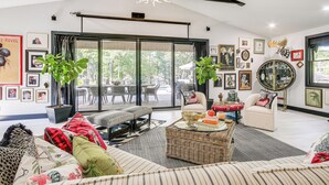 Ein geräumiges Wohnzimmer mit großem Fenster, einer Kristallleuchtre und verschiedenen gerahmten Bildern an den Wänden.
