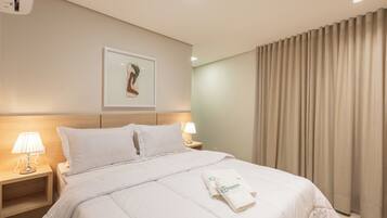 A hotel room with a neatly made bed, a framed artwork on the wall, and a window with curtains.