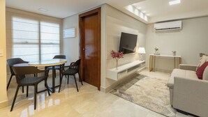 A modern living room with a dining area, a flat-screen TV, a sofa, and a small table with a lamp. - Maranatha Suítes (Campo Grande)