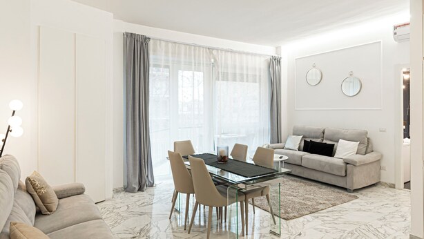 Uma sala de estar moderna com piso de mármore, um sofá, uma mesa de jantar com cadeiras e uma janela grande com cortinas.