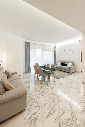 A modern living room with a marble floor, a sofa, a dining table with chairs, and a large window with curtains. - Trastevere 6, Casa Malupa Trastevere 6 (Roma)