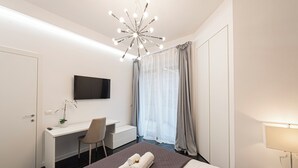 Quarto de hotel moderno com cama, secretária, cadeira, televisão e janela com cortinas.