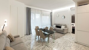 Uma sala de estar moderna com uma mesa de jantar de vidro, um sofá e uma cozinha com geladeira.