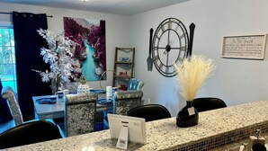 A hotel reception area with a granite counter, a clock, a framed sign, and a painting of a river. - Family-Friendly 3BR/3BA Gainesville Condo Near Downtown & Lake (Gainesville)