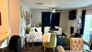A modern living room with a white sofa, a green armchair, a glass coffee table, and a fireplace. - Family-Friendly 3BR/3BA Gainesville Condo Near Downtown & Lake (Gainesville)