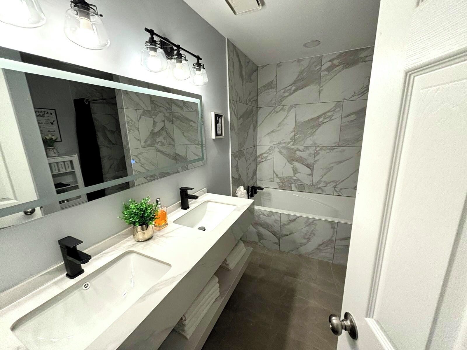 Une salle de bain moderne avec deux vasques, un grand miroir et des murs à motifs de marbre.