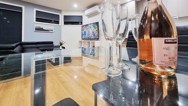 Ein modernes Wohnzimmer mit einem Glastisch, einer Flasche Kirkland Prosecco und drei Weingläsern.